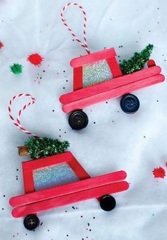 two red wooden toy cars decorated with glitter and christmas tree decorations on top of white paper