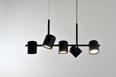 three black lamps hanging from the ceiling with white walls behind them and one light on each side