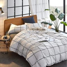 a bed with white and black comforter next to a window in front of a potted plant