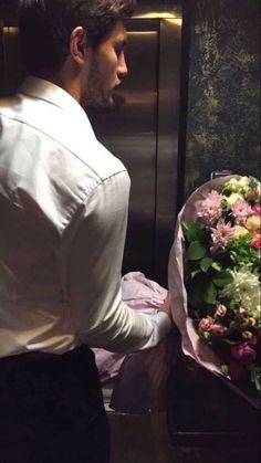 a man holding a bouquet of flowers in front of a metal wall with an elevator behind him