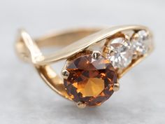 an orange and white diamond ring sitting on top of a gray surface with gold accents