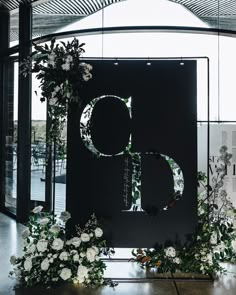 the letter d is surrounded by flowers and greenery in front of a large window