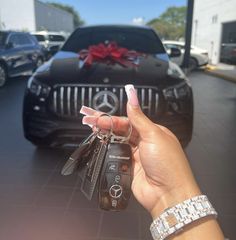 a hand holding keys in front of a car with a red bow on the hood