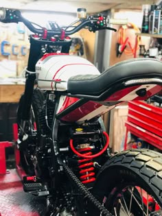 a red and white motorcycle is parked in a garage with other tools on the wall