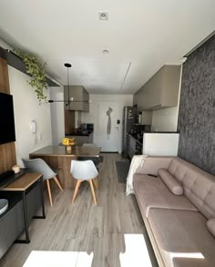 a living room and kitchen area in a small apartment with wood flooring, white walls and furniture