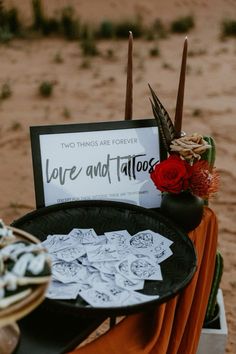 there is a sign that says love and tattoos next to some flowers on a table