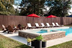 a pool with lounge chairs and umbrellas next to a fenced in backyard area