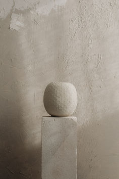 a white ball sitting on top of a cement block in front of a stucco wall