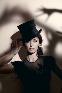 a woman wearing a black top hat with her hands in the air and shadows on the wall behind her