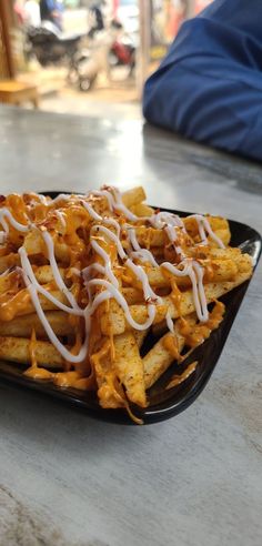 a black plate topped with cheesy french fries covered in cheese and drizzled