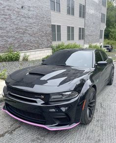 a black car with pink stripes parked in front of a brick building