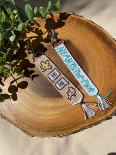 two cross stitch keychains sitting on top of a tree stump next to a plant