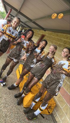 a group of people standing next to each other in front of a wall with mud on them