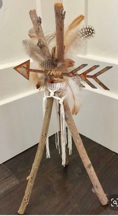 an arrangement of sticks and feathers on top of a wooden tripod in front of a white wall