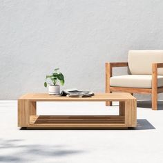 a wooden coffee table sitting on top of a white floor next to a chair and potted plant