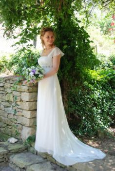 a woman in a white dress standing next to a stone wall