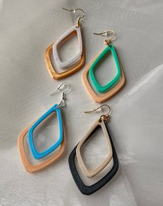 three pairs of wood and plastic earrings on a white surface, with one pair dangling from the ear