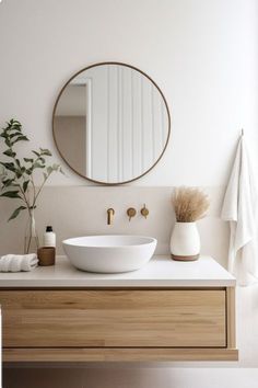 a white sink sitting under a round mirror next to a wooden cabinet and counter top