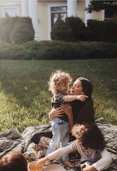 a woman holding a child while sitting on top of a blanket in front of a house