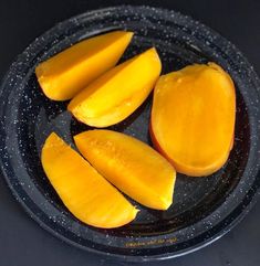 sliced mangoes in a black bowl on a dark table top, ready to be eaten