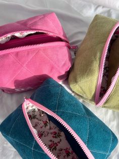 three zippered pouches sitting on top of a bed with white sheets and pillows