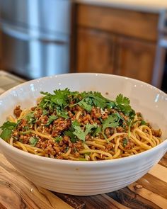 a white bowl filled with noodles and meat on top of a wooden table next to a pot