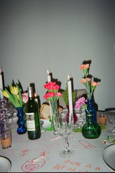 a table topped with lots of vases filled with flowers next to bottles and glasses