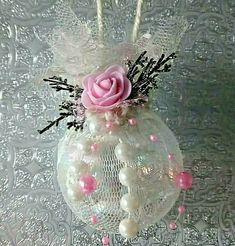 a glass ornament with a pink rose in it on a lace doily