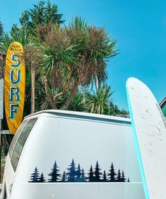 there is a surfboard leaning up against the car window and it has trees painted on it