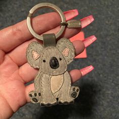 a hand holding a metal keychain with a koala on it