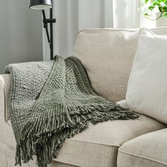 a couch with a blanket on top of it next to a lamp and window sill