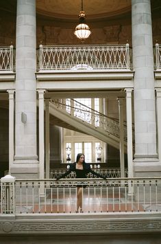 a woman standing on top of a balcony next to a stair case in a building