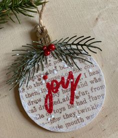 a christmas ornament with the word joy on it hanging from a pine tree