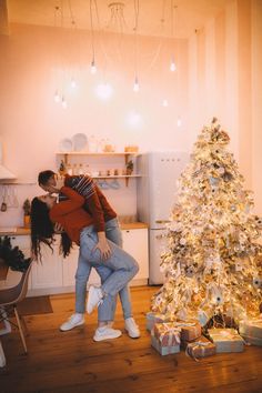 two people kissing in front of a christmas tree