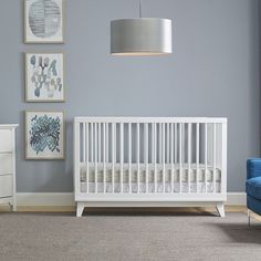 a white crib in a room with blue chairs and pictures on the wall behind it