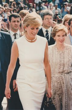 two women in white dresses walking next to each other with men in suits and ties behind them