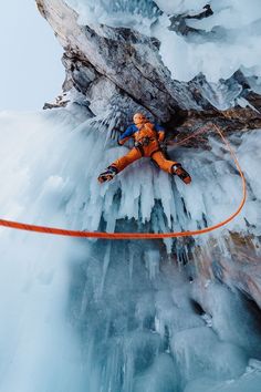 a man climbing up the side of a snow covered mountain next to an orange rope