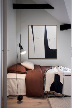 a bed sitting in a bedroom next to a lamp on a wooden floor and white walls