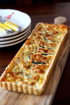 a quiche on a wooden board next to plates and utensils