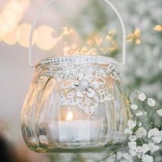 a candle is lit in a glass jar with lace on the handle and flowers around it