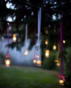 some lights hanging from a tree outside in the night time with pink ribbon around them