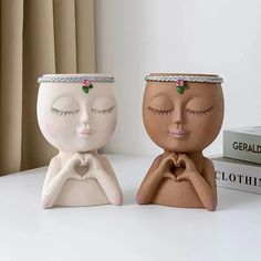 two ceramic pots sitting on top of a table next to each other with eyes closed