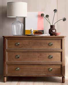 a chest of drawers with vases and flowers on top, next to a lamp