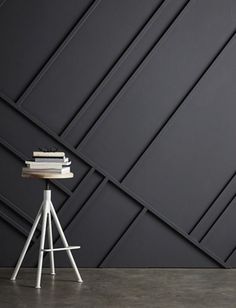 a white chair sitting next to a table with books on top of it in front of a black wall