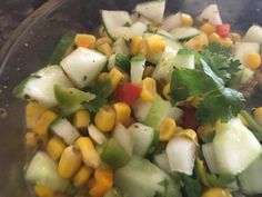 a glass bowl filled with corn, cucumber and cilantro