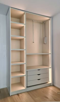 an empty white closet with drawers and lights on the shelves, in front of a door