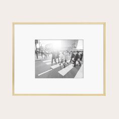 a black and white photo of people walking across a crosswalk with the sun shining down on them