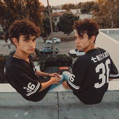 two young men sitting next to each other on top of a skateboard ramp in front of a parking lot