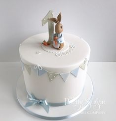 a white cake with a blue ribbon around it and a rabbit figurine on top