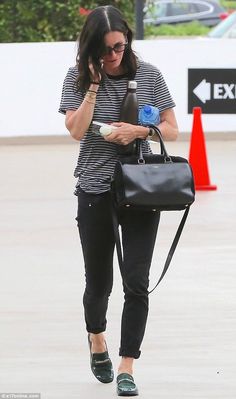 a woman is walking while talking on her cell phone and holding a black bag in her hand